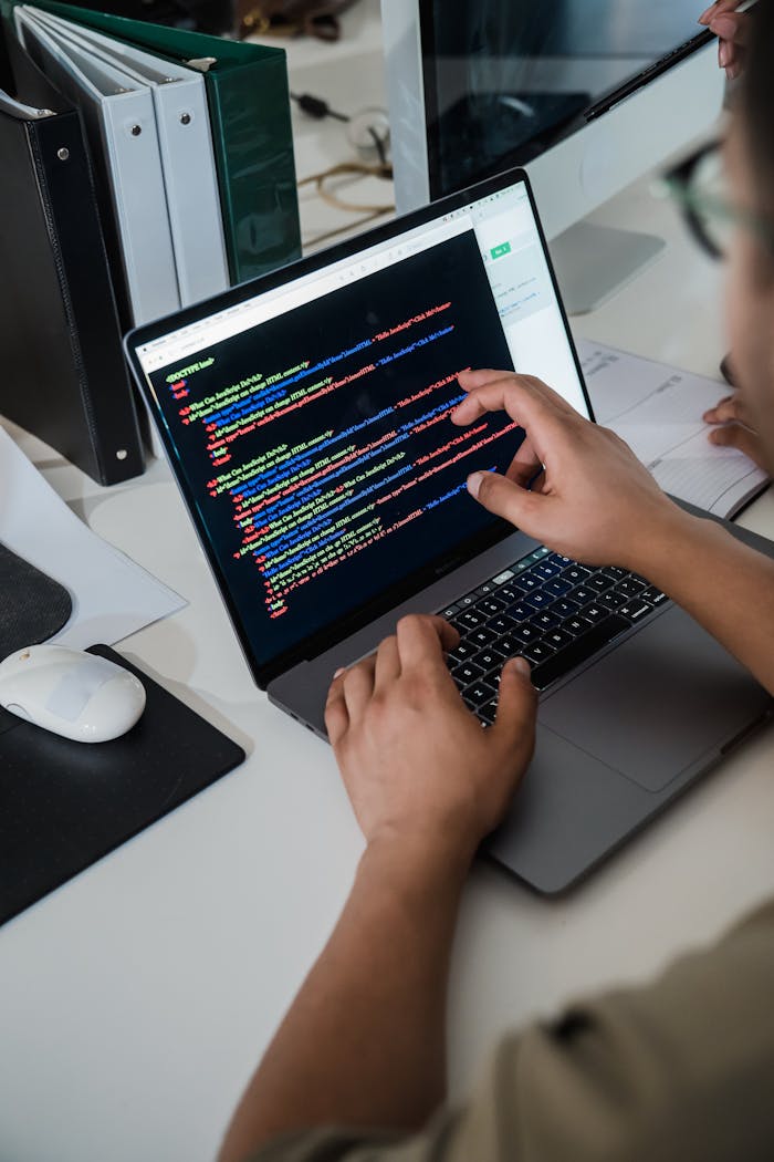 services-03 Close-up of a programmer pointing at a colorful code script on a laptop in an office setting.
